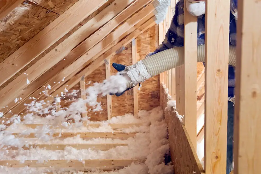 Contractor blowing loose-fill insulation into attic rafter bays